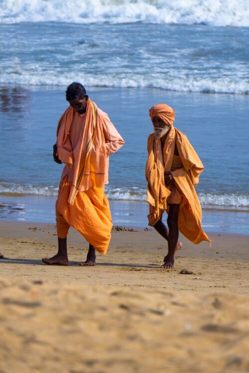 pilgrims in orange robes walking on the beach in puri india